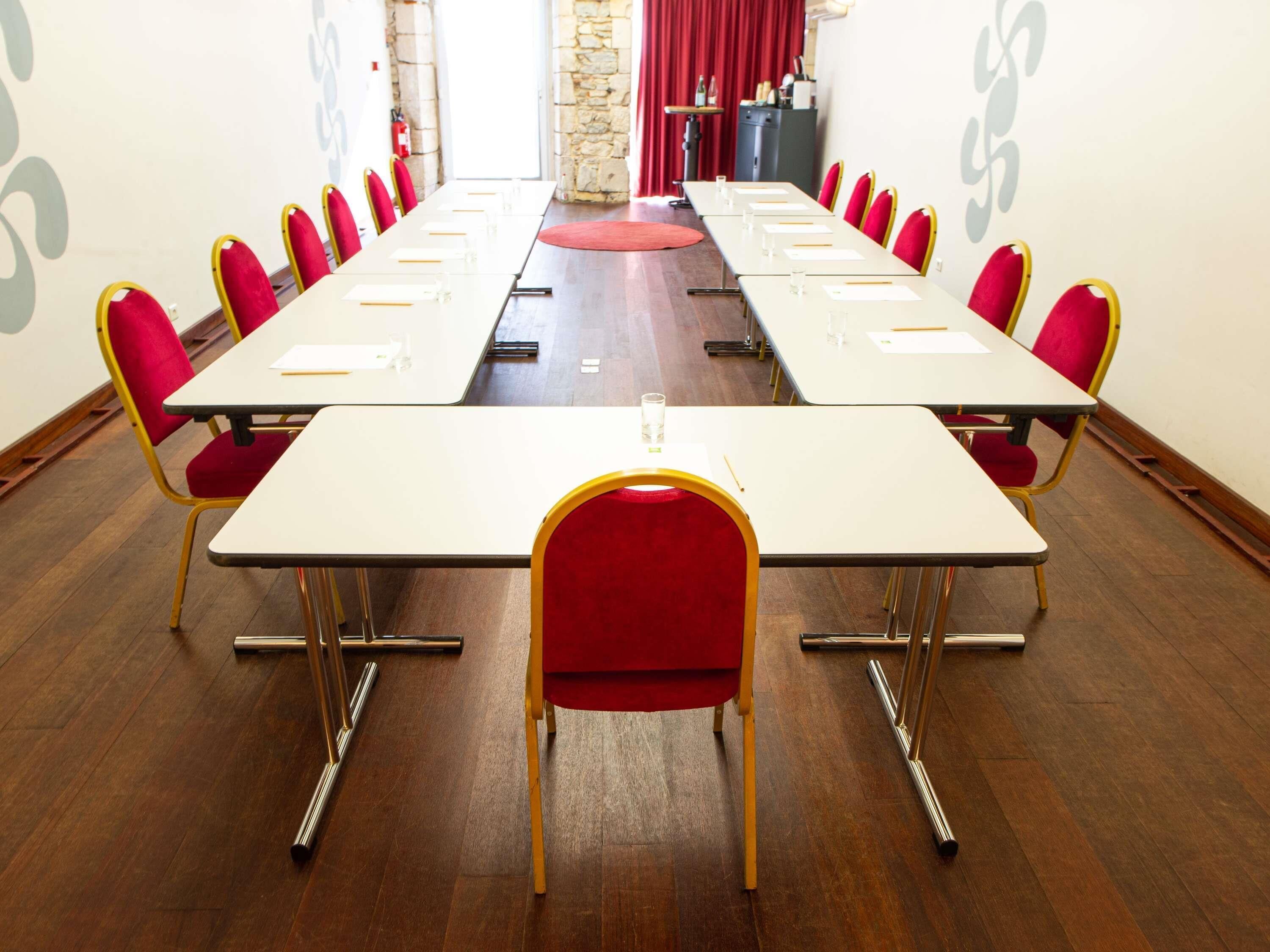 A conference room with long tables, red chairs, and a stone wall.