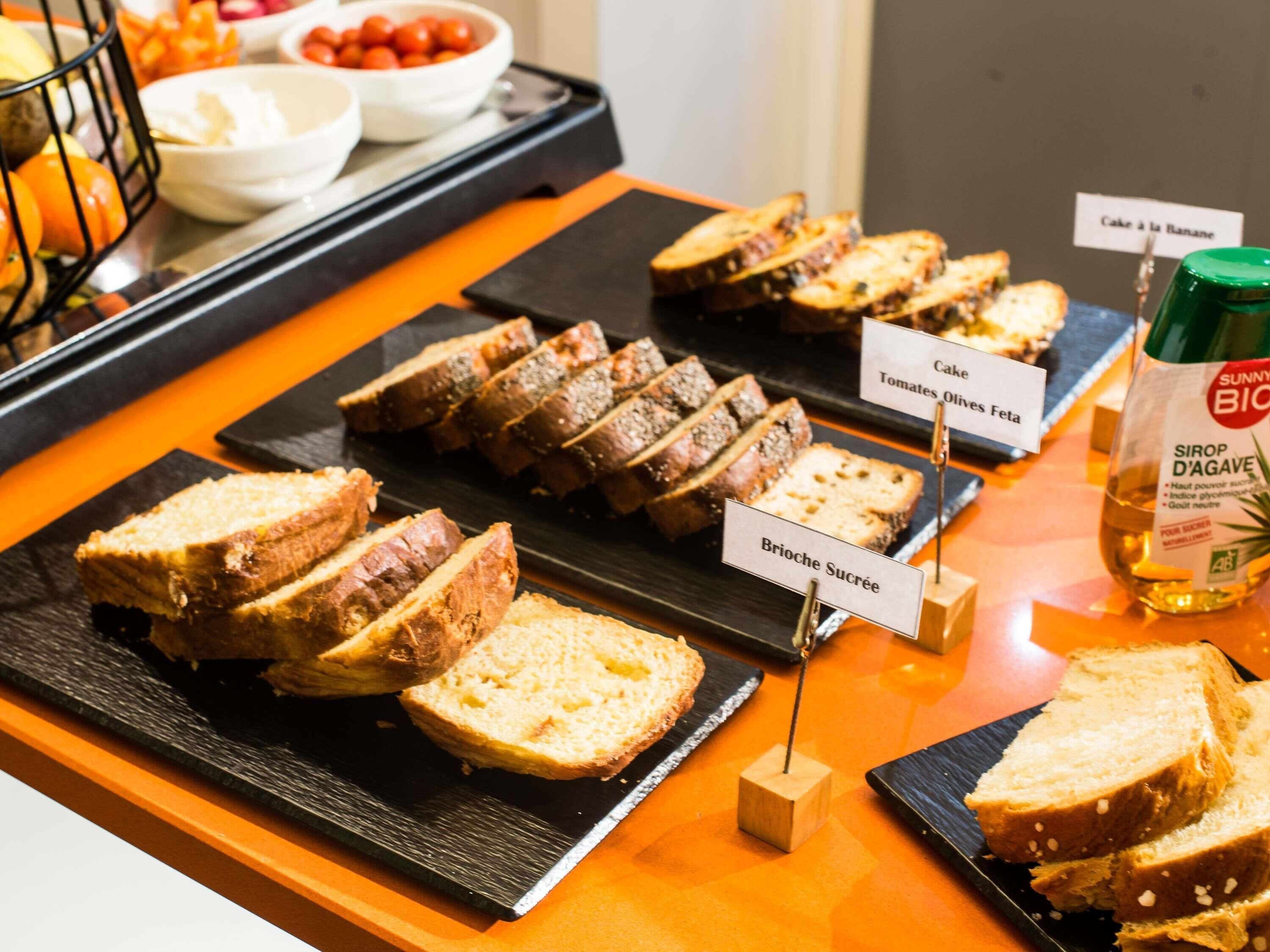 Un bufé con diversas opciones de pan y pastel, incluyendo brioche y pastel con tomates y aceitunas.