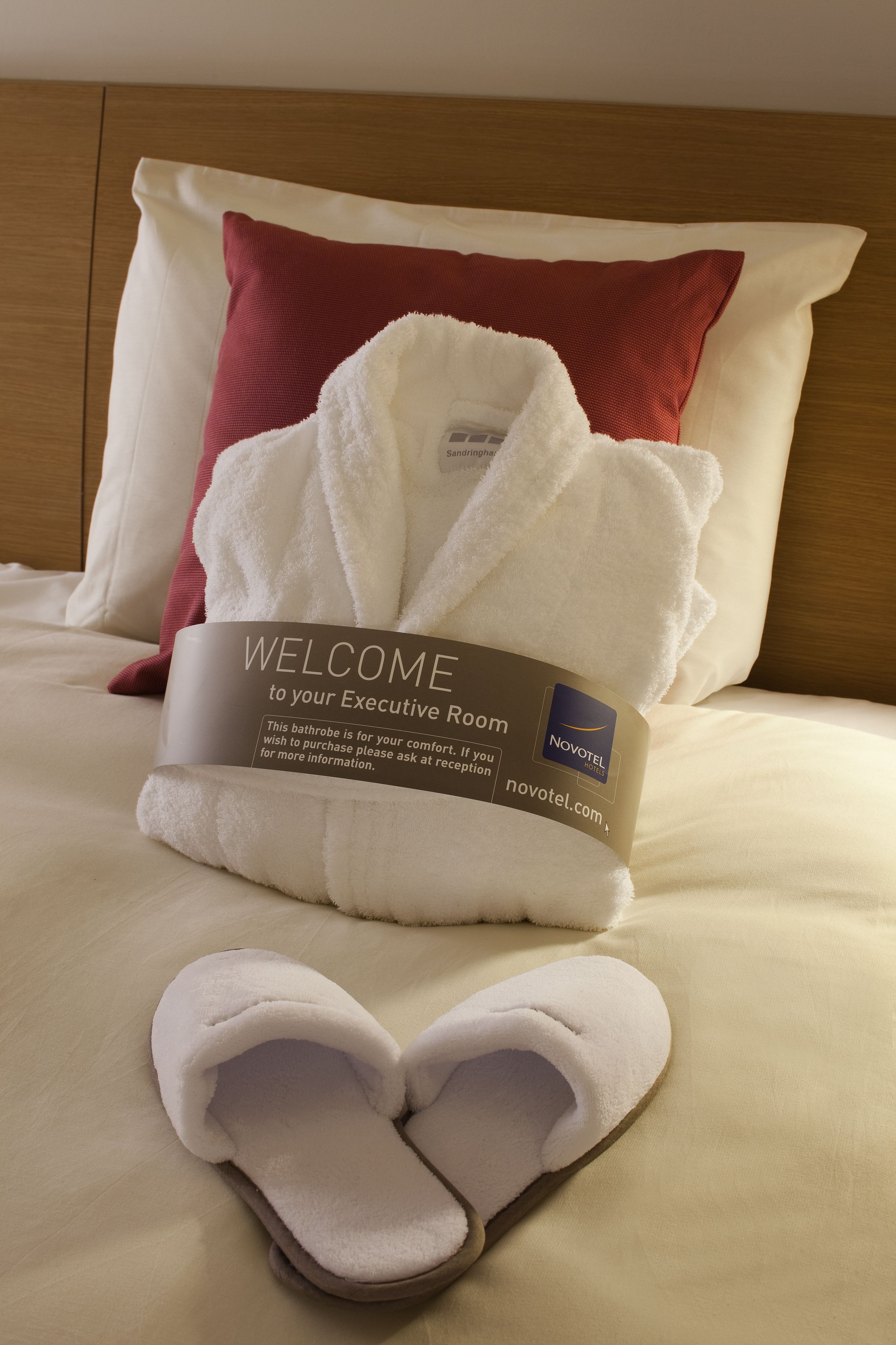 A neatly made bed with a welcome mat, slippers, and a pillow.