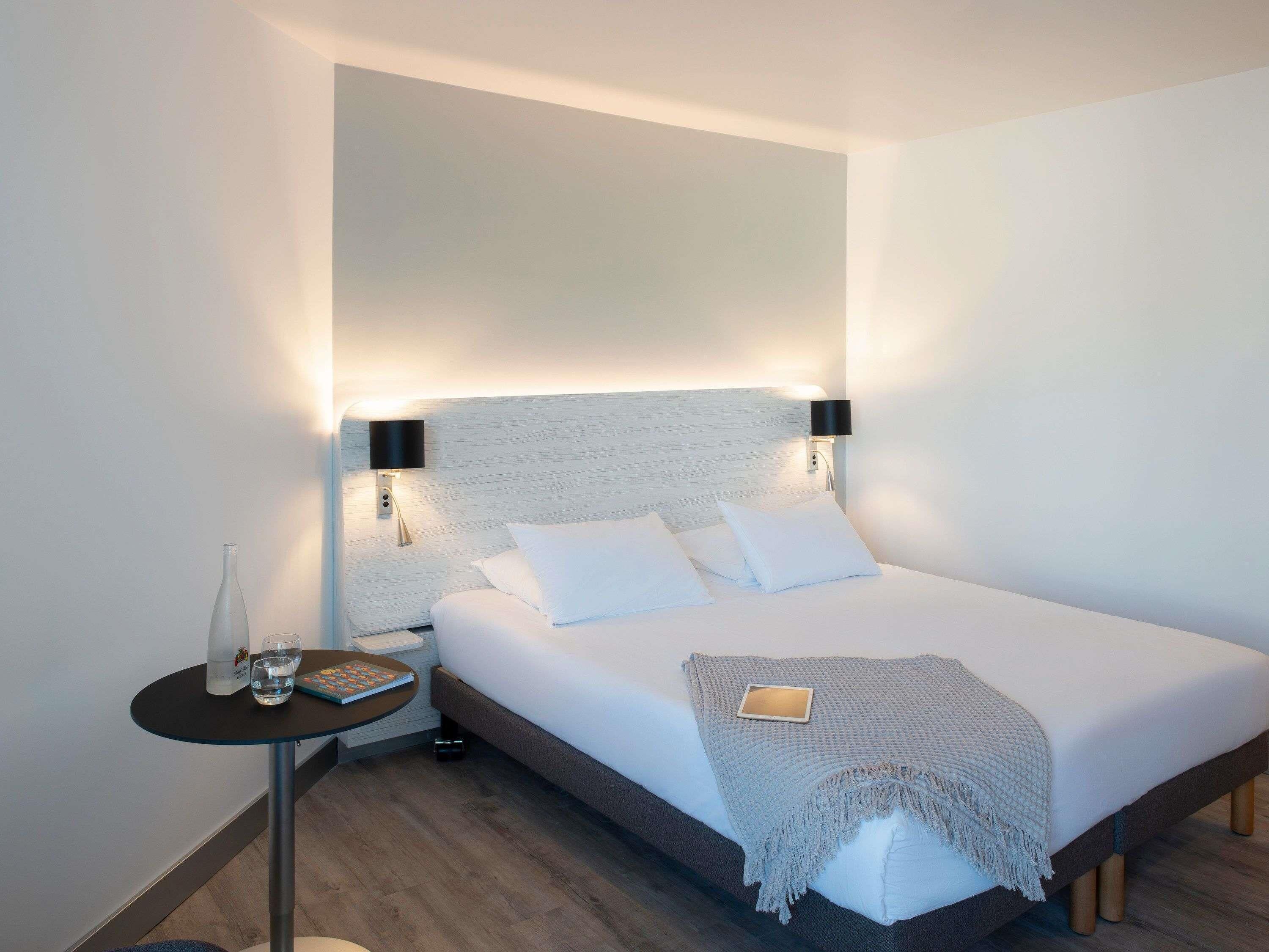 Una habitación de hotel moderna con una cama grande, mesitas de noche y una lámpara de noche.