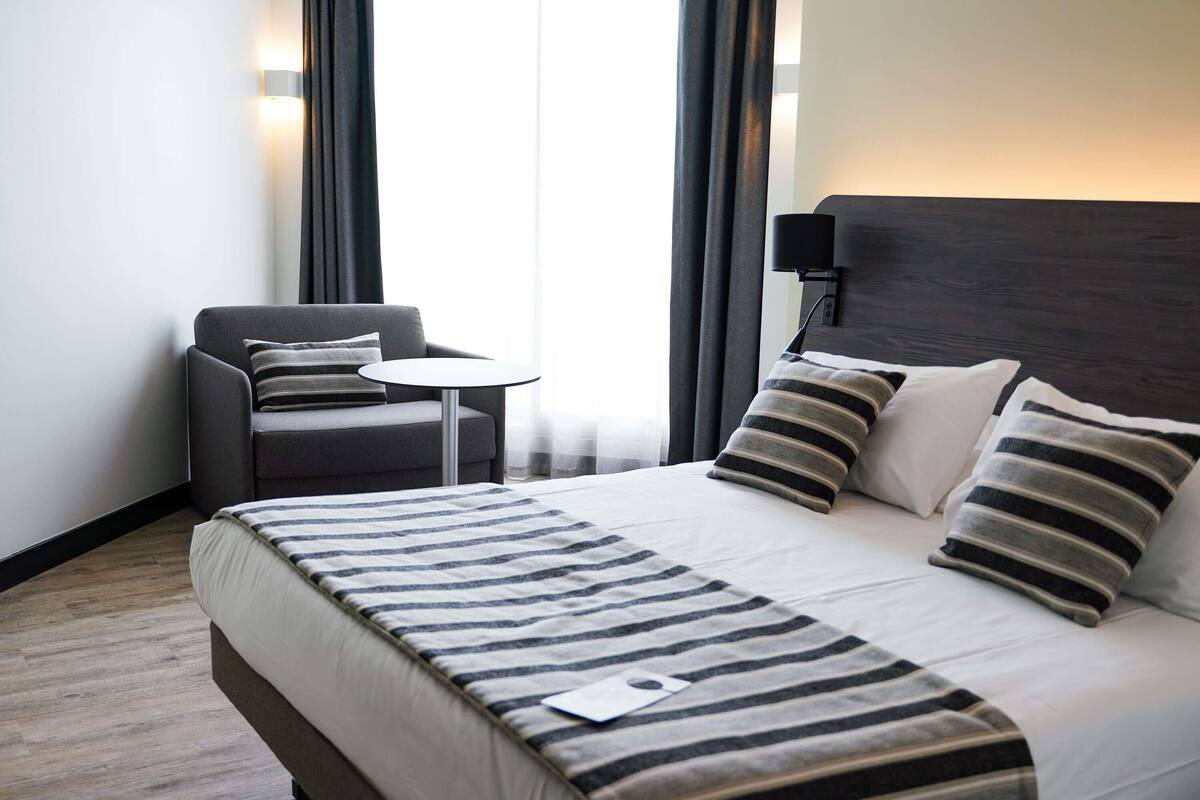 Ein Hotelzimmer mit einem Bett, einem Sessel, einem kleinen Tisch und einer Lampe.