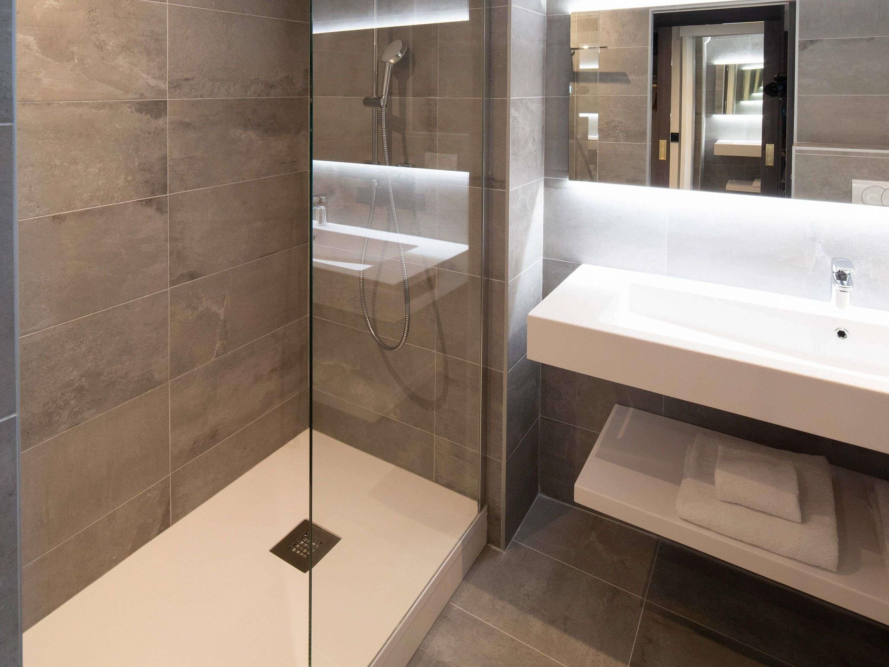 A modern bathroom with a glass-enclosed shower, a white sink, and a mirror.