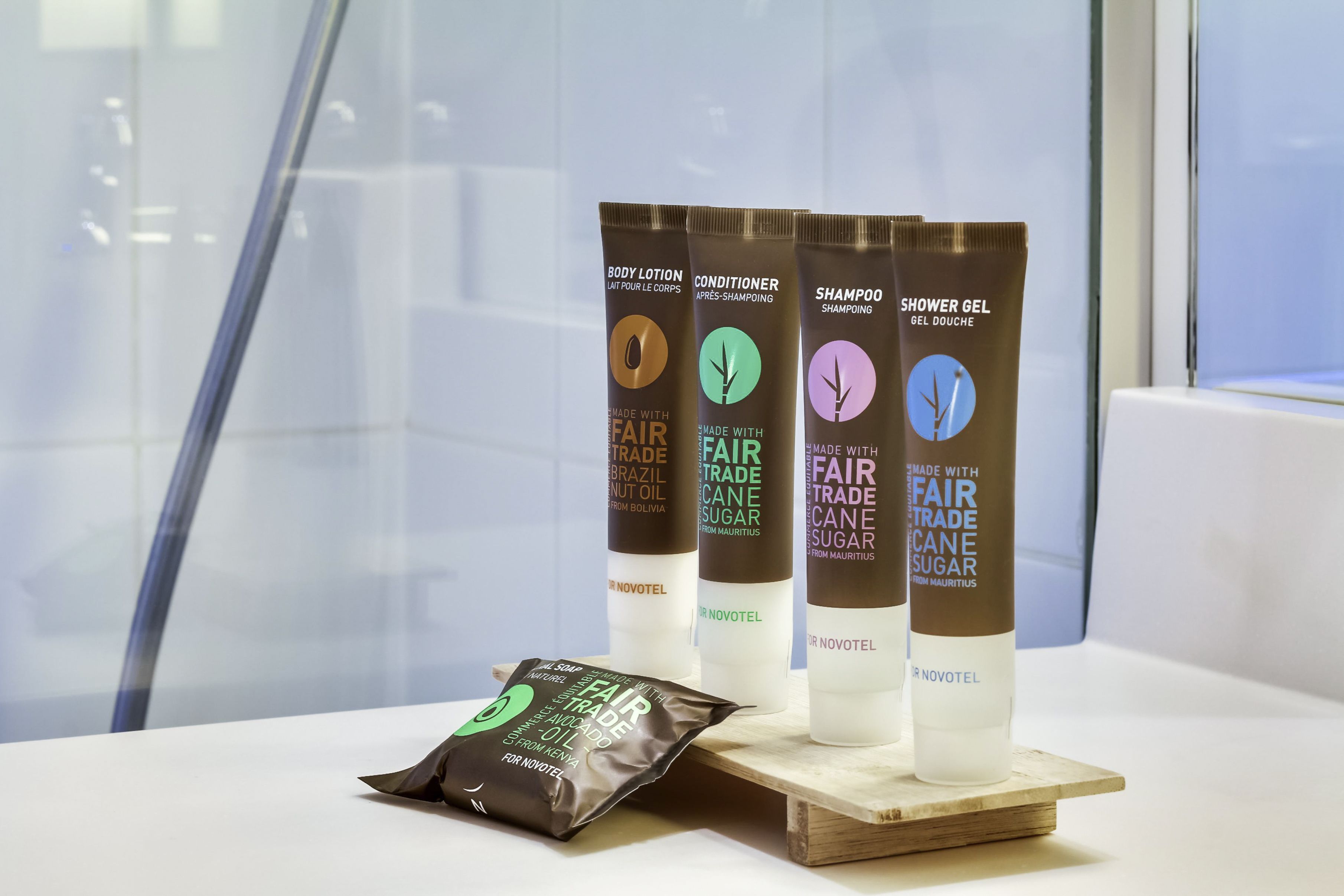 Exposição de artigos de higiene pessoal do hotel Novotel, incluindo loção corporal, condicionador e shampoo.