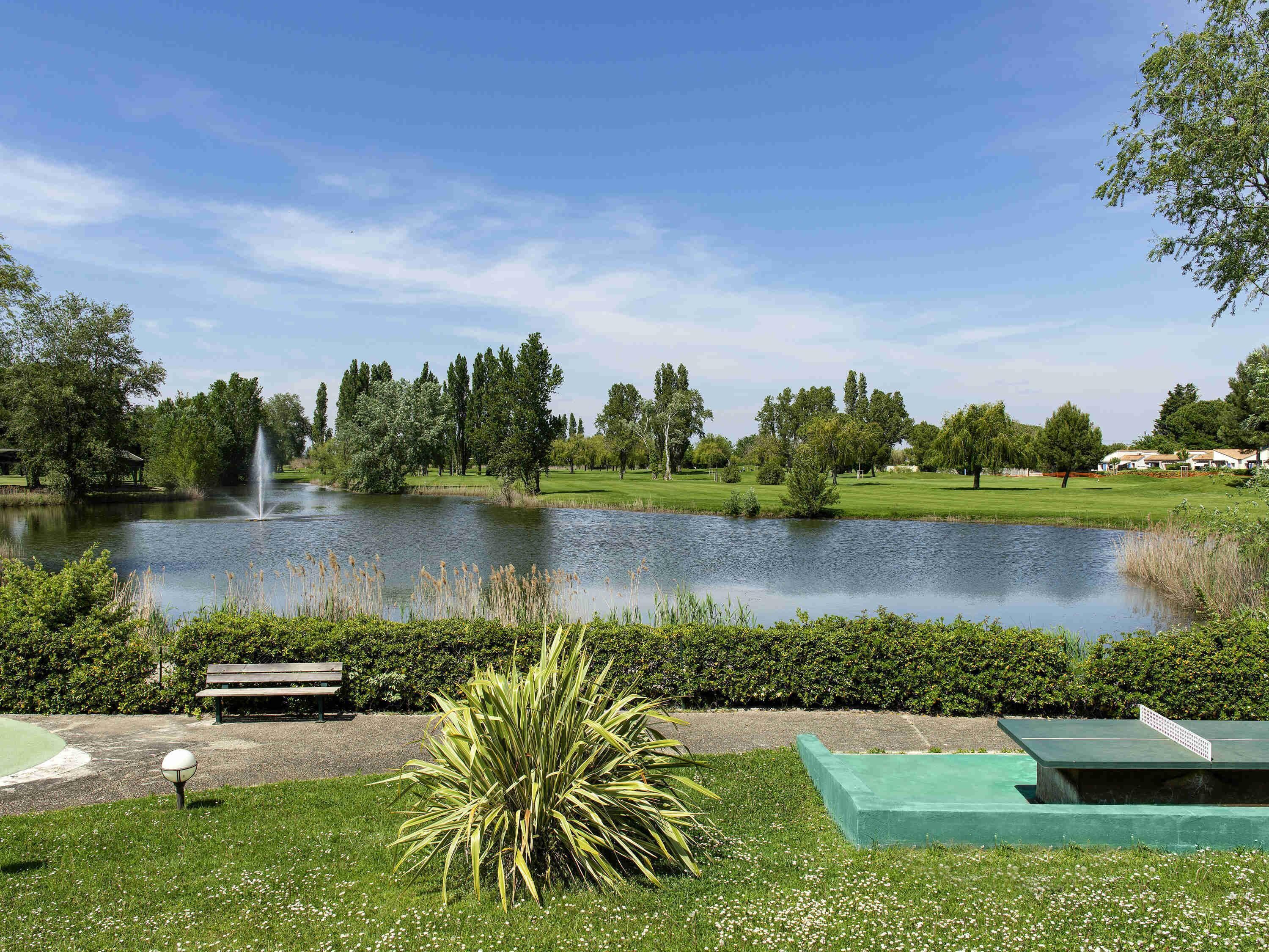 Eine friedliche Außenanlage mit Teich, Brunnen, Tennisplatz und Golfplatz im Hintergrund.