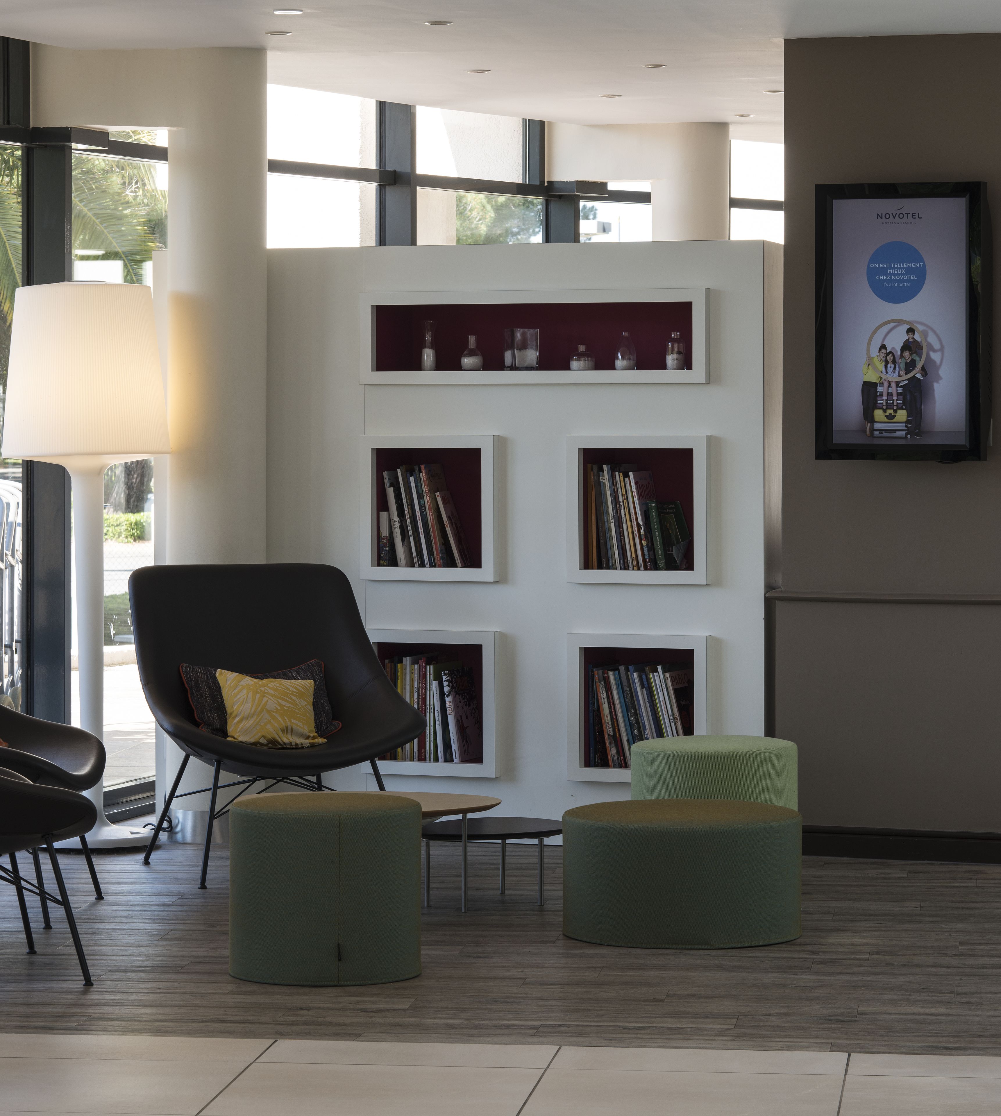 A modern lobby with a black armchair, green ottoman, and a white bookshelf with books and decorative items.