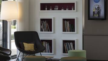 A modern lobby with a black armchair, green ottoman, and a white bookshelf with books and decorative items.