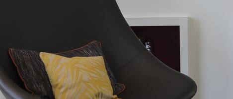 Une pièce moderne avec une chaise noire, un coussin jaune, une petite table ronde et une bibliothèque adossée au mur.