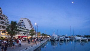 Un port de plaisance avec des bateaux amarrés, une foule de personnes et un immeuble doté de balcons.