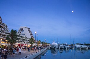 Un port de plaisance avec des bateaux amarrés, une foule de personnes et un immeuble doté de balcons.