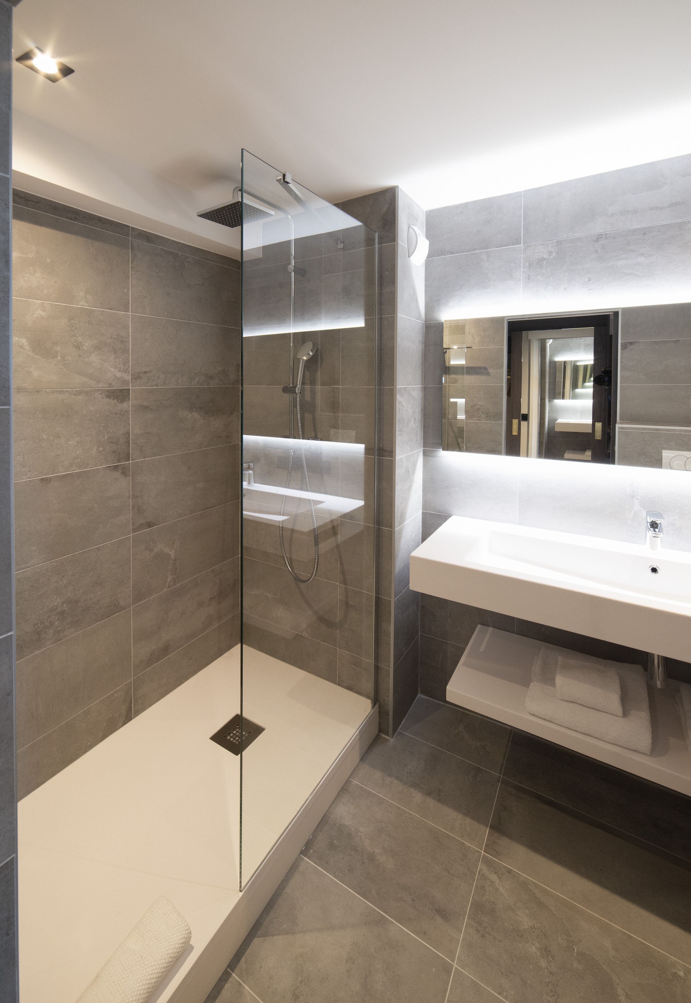 Un baño moderno con ducha de vidrio, un lavamanos espacioso y un espejo sobre él.