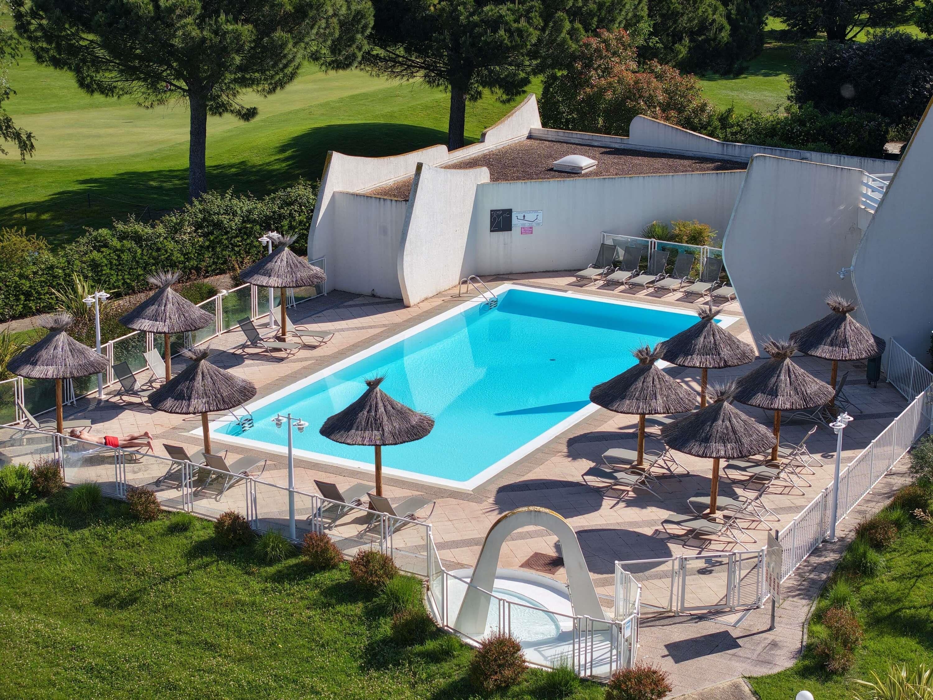 Uma piscina com espreguiçadeiras e guarda-sóis, cercada por um edifício branco com uma bandeira.