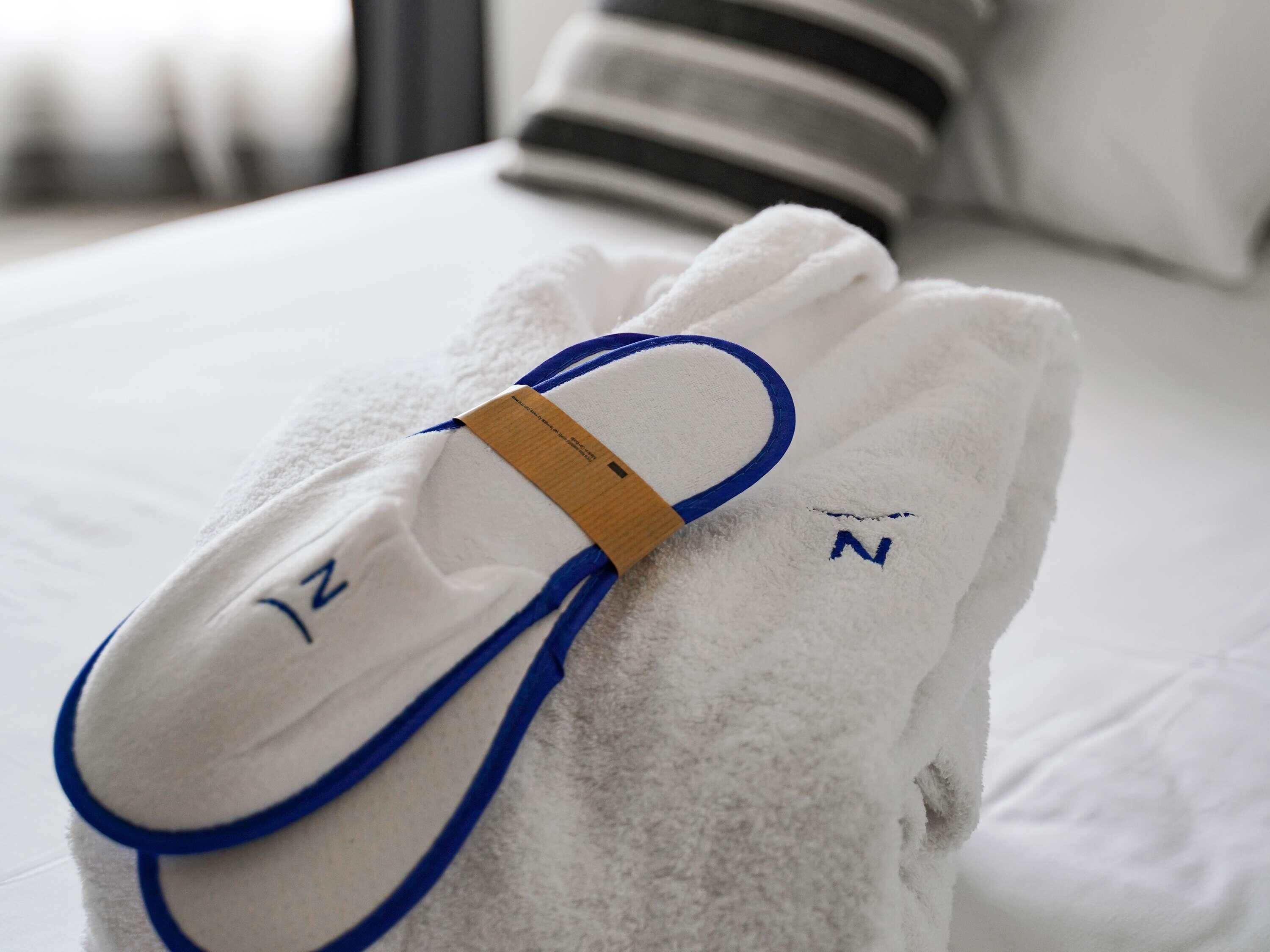 Ein weißes Handtuch mit blauem Henkel und einem Etikett auf einem Bett.