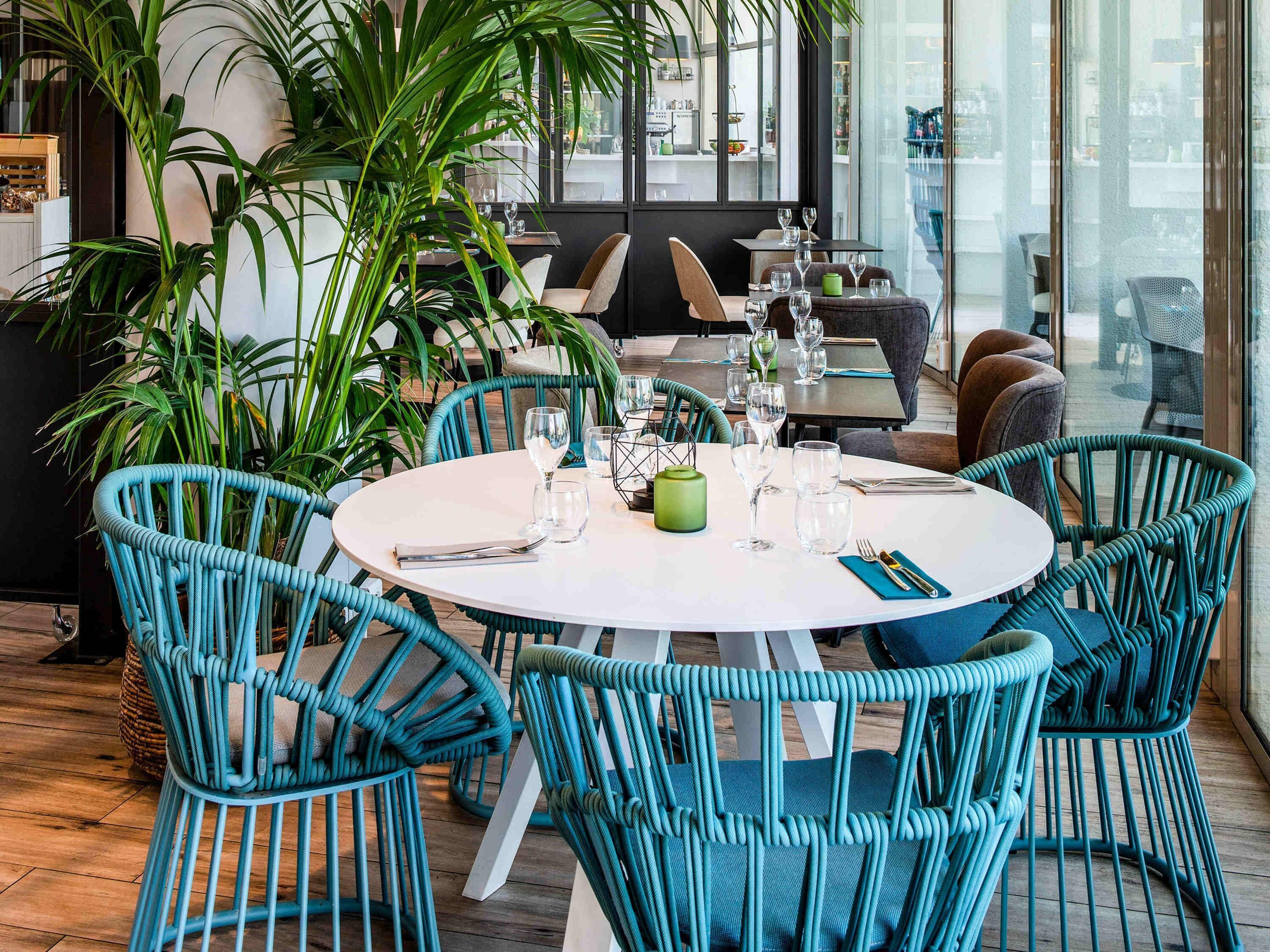 A dining area with round tables, teal chairs, and a large potted plant.