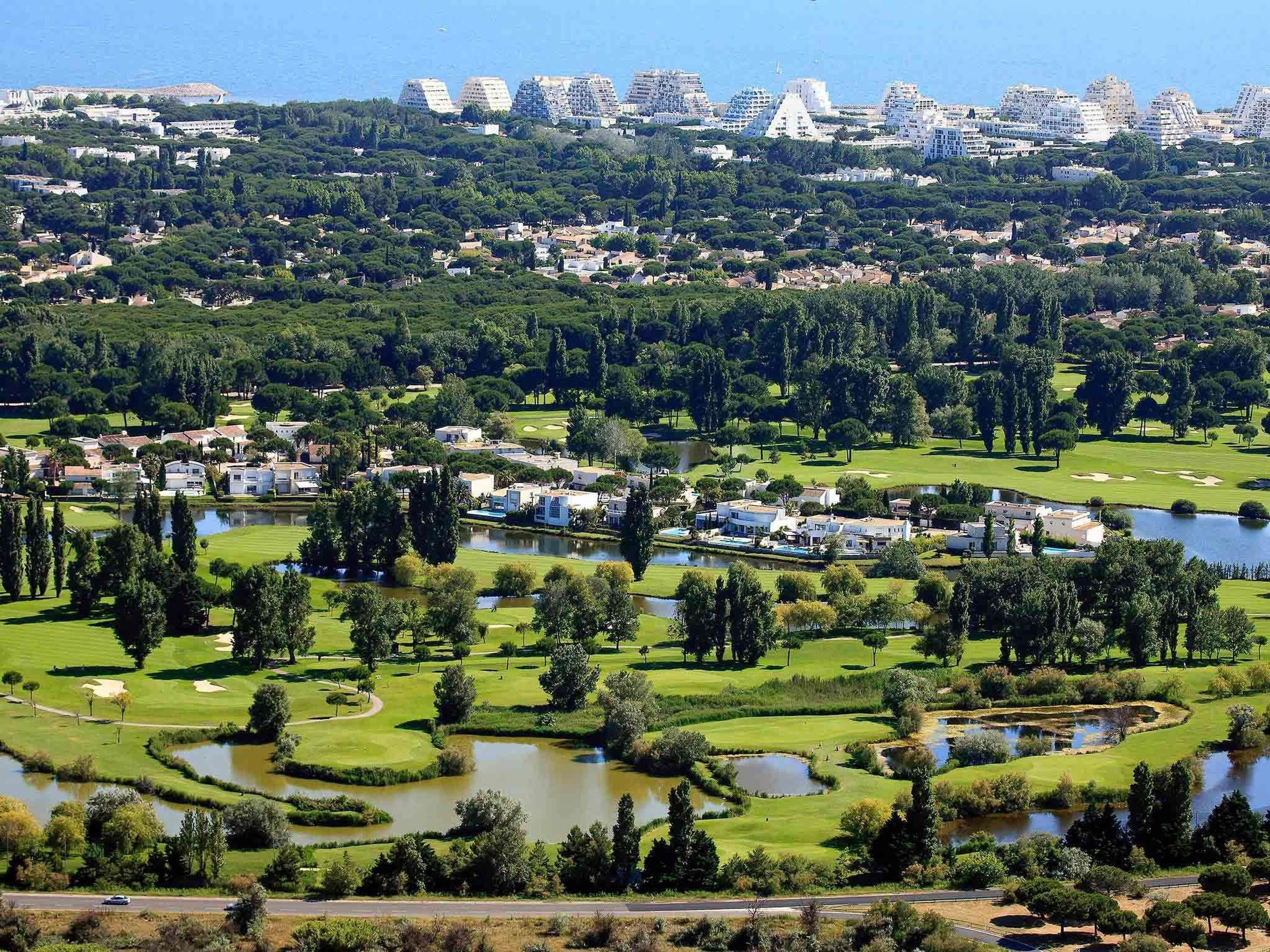A golf course with a lake, surrounded by residential buildings and greenery.