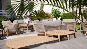 Un espace extérieur aménagé avec des meubles en osier et une table en bois, le tout entouré de verdure.