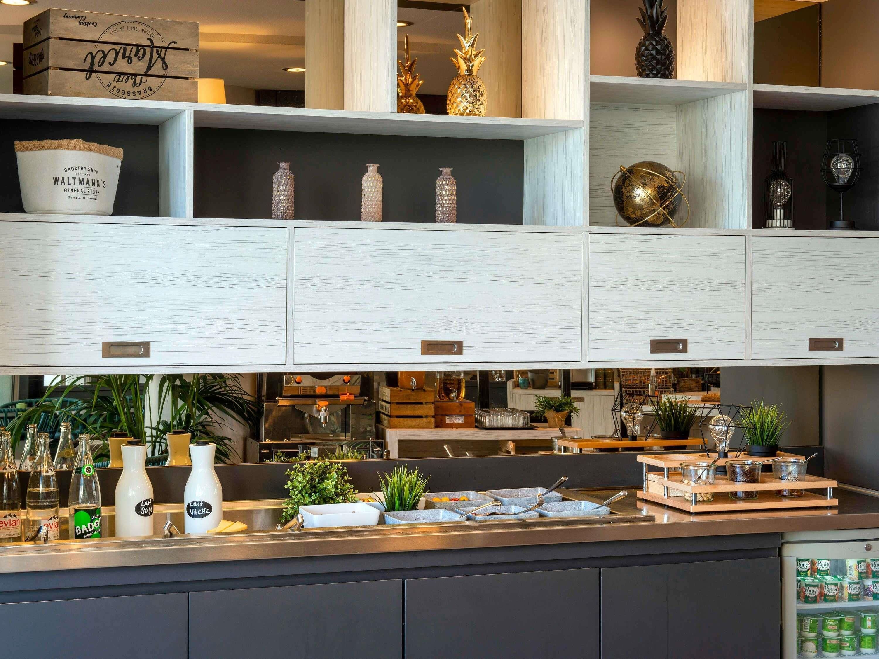 A kitchen with white cabinetry, a countertop with various bottles, and a refrigerator stocked with products.
