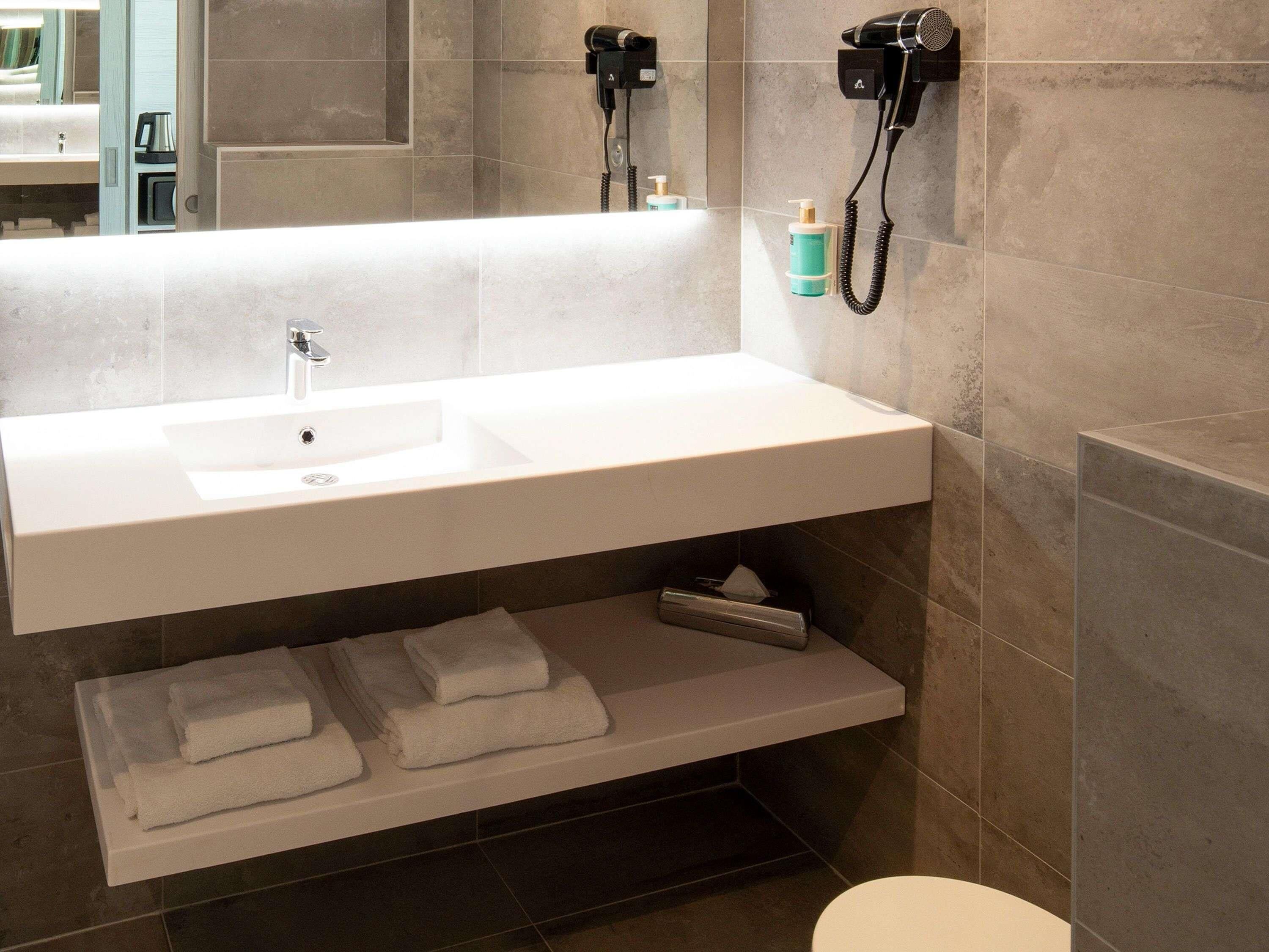 A modern bathroom with a white sink, towel rack, and a hairdryer mounted on the wall.