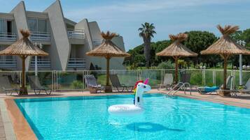 Relax by the pool surrounded by lounge chairs and shaded umbrellas, with a whimsical unicorn decoration.