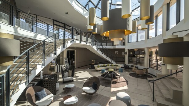 Un hall d’entrée spacieux avec un plafond haut, de nombreux espaces de détente et un escalier menant aux étages supérieurs.
