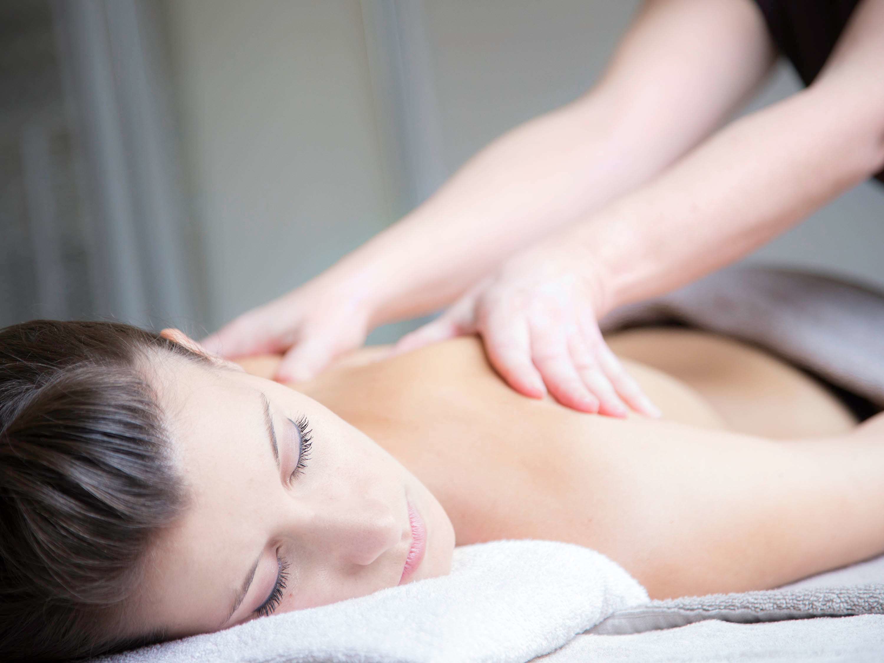 A person receiving a back massage in a room with a plain wall and a window.