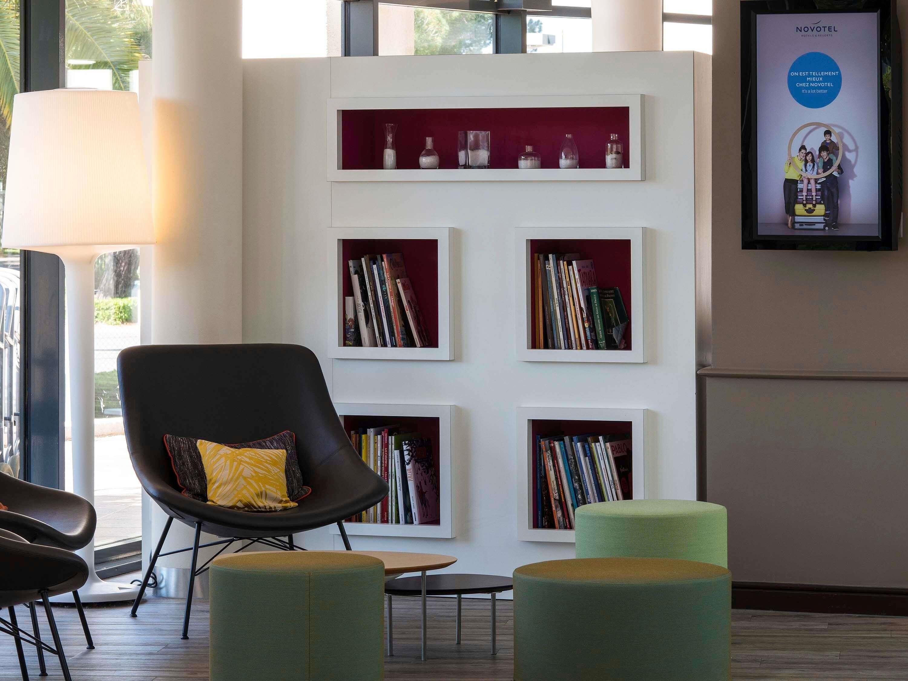A modern hotel lobby with a black chair, green ottomans, and a bookshelf with books.