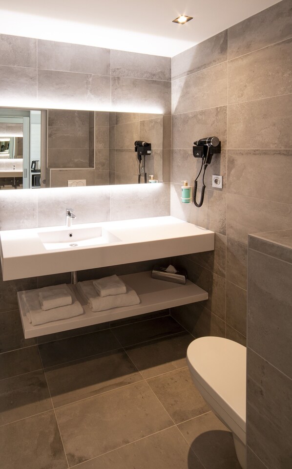 A modern bathroom with a large mirror, a white sink, a hairdryer, and a toilet.