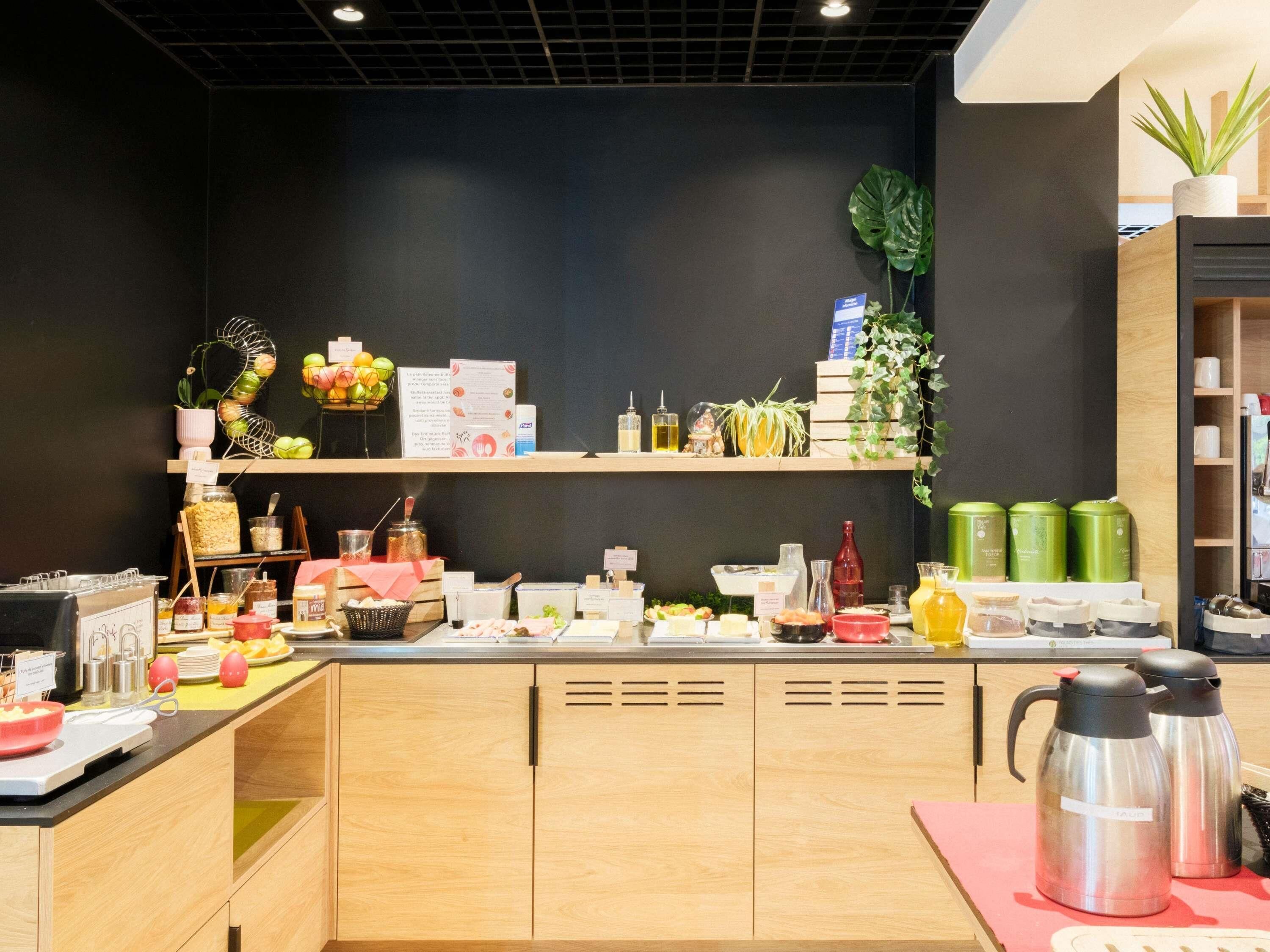 A modern kitchen with wooden cabinets, a coffee station, and various food items on display.