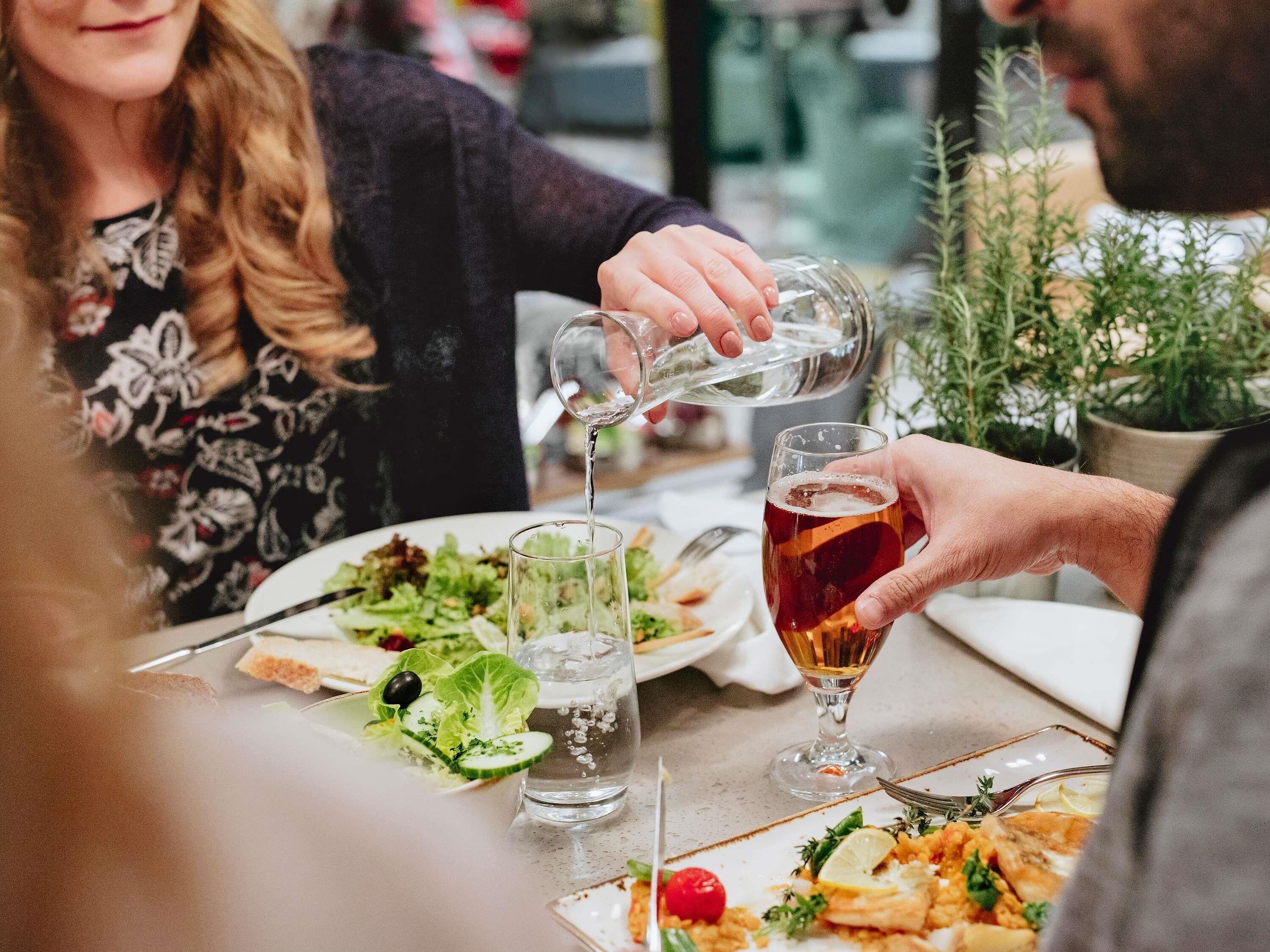 A dining table with plates of food, glasses, and a person pouring a drink.