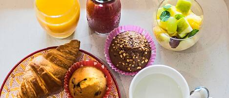 Bandeja de desayuno con croissants, muffins, un vaso de jugo de naranja, un bol de fruta y una taza de café.