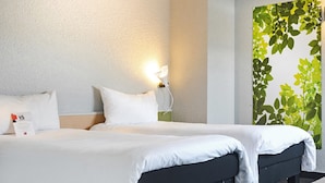 A hotel room with a large bed, two pillows, a bedside table, a wall-mounted lamp, and a green leafy wall decoration. - ibis Strasbourg Sud La Vigie (Ostwald)