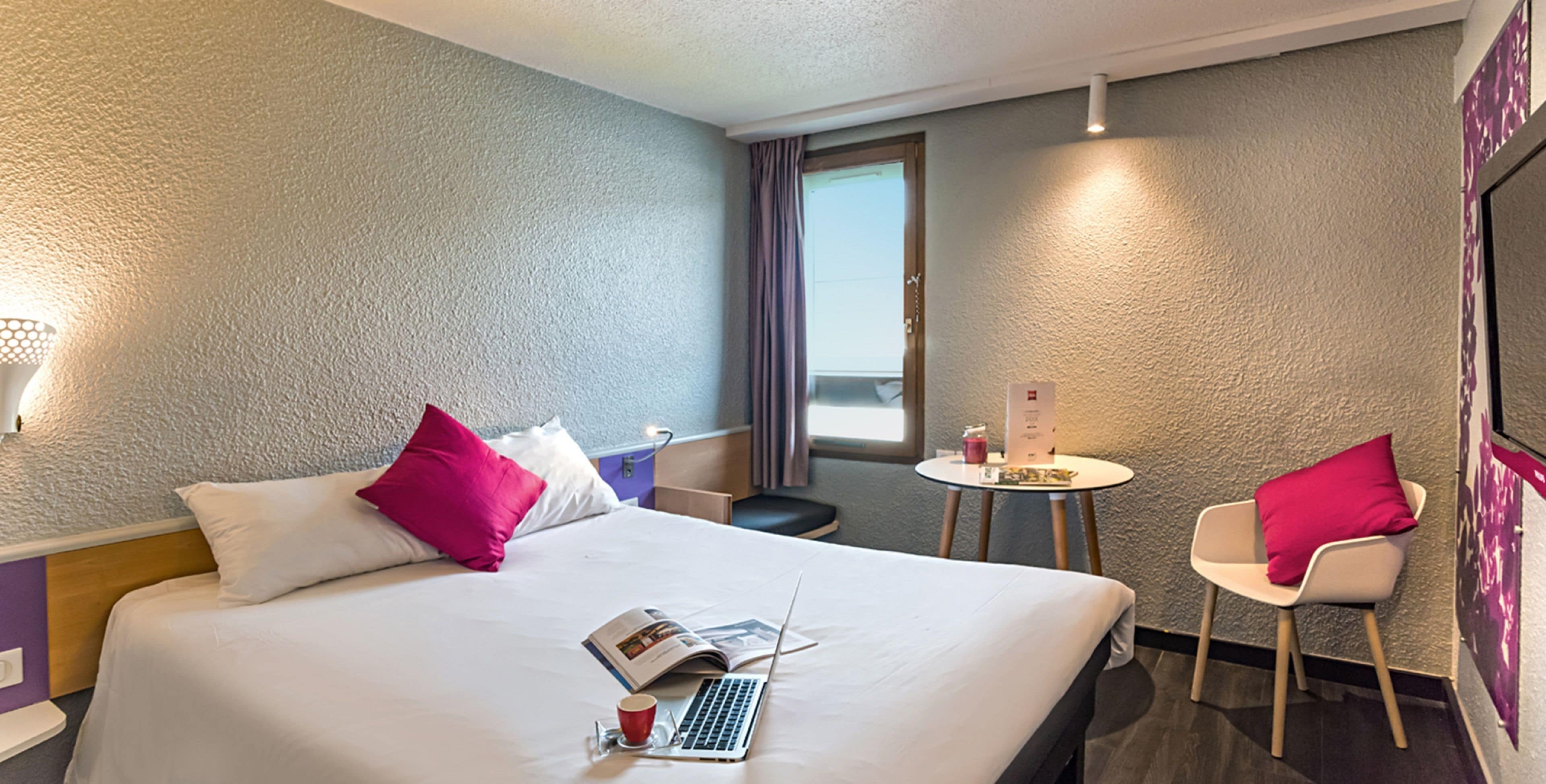 Quarto de hotel com uma cama, um laptop, uma chávena e uma cadeira.