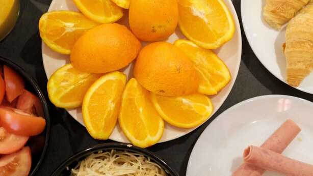 Ein Tisch mit verschiedenen Speisen, darunter Orangen, Tomaten und ein Teller mit einem Croissant.