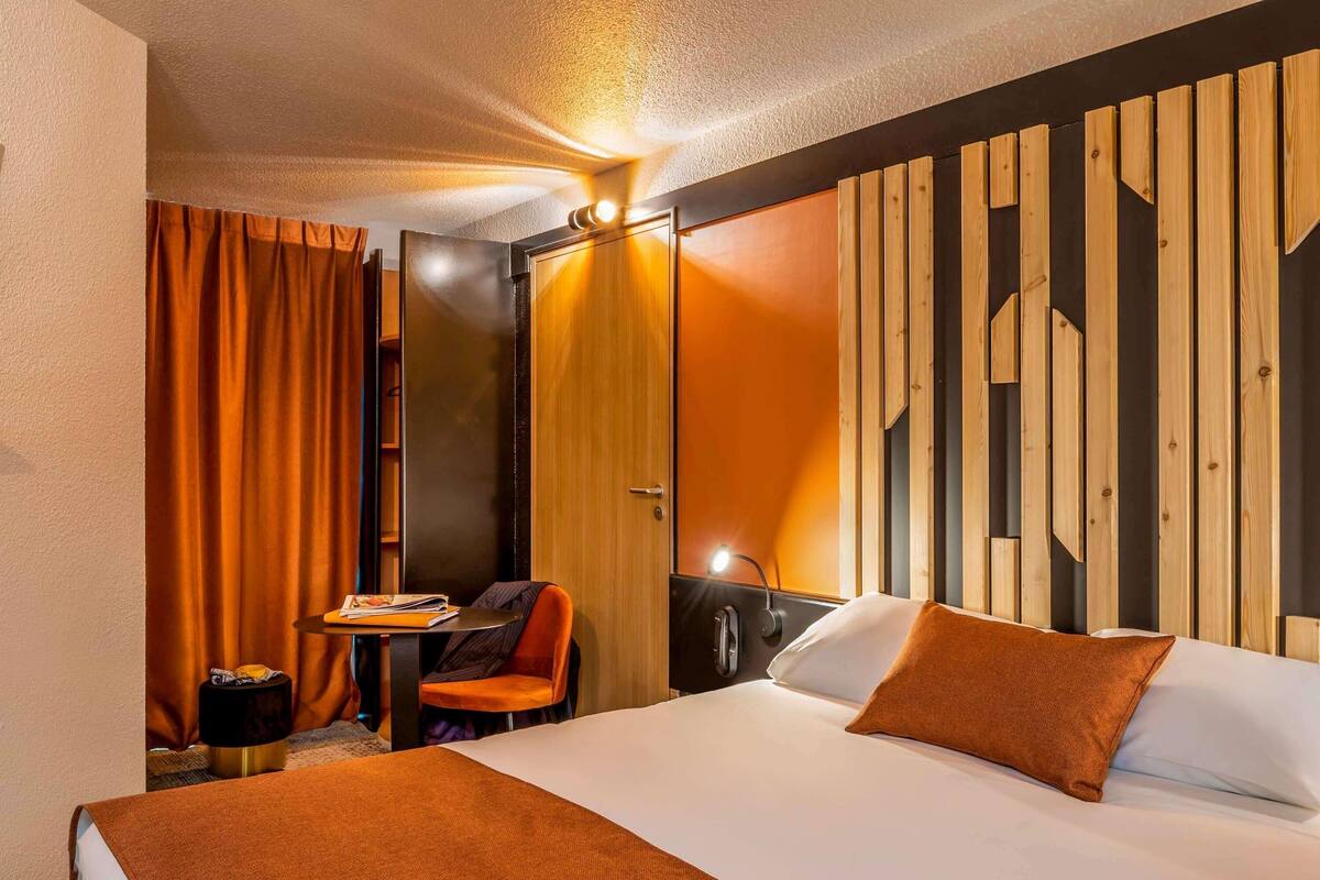 Una camera d'albergo con un letto, un tavolino con una sedia e un divisorio in legno.