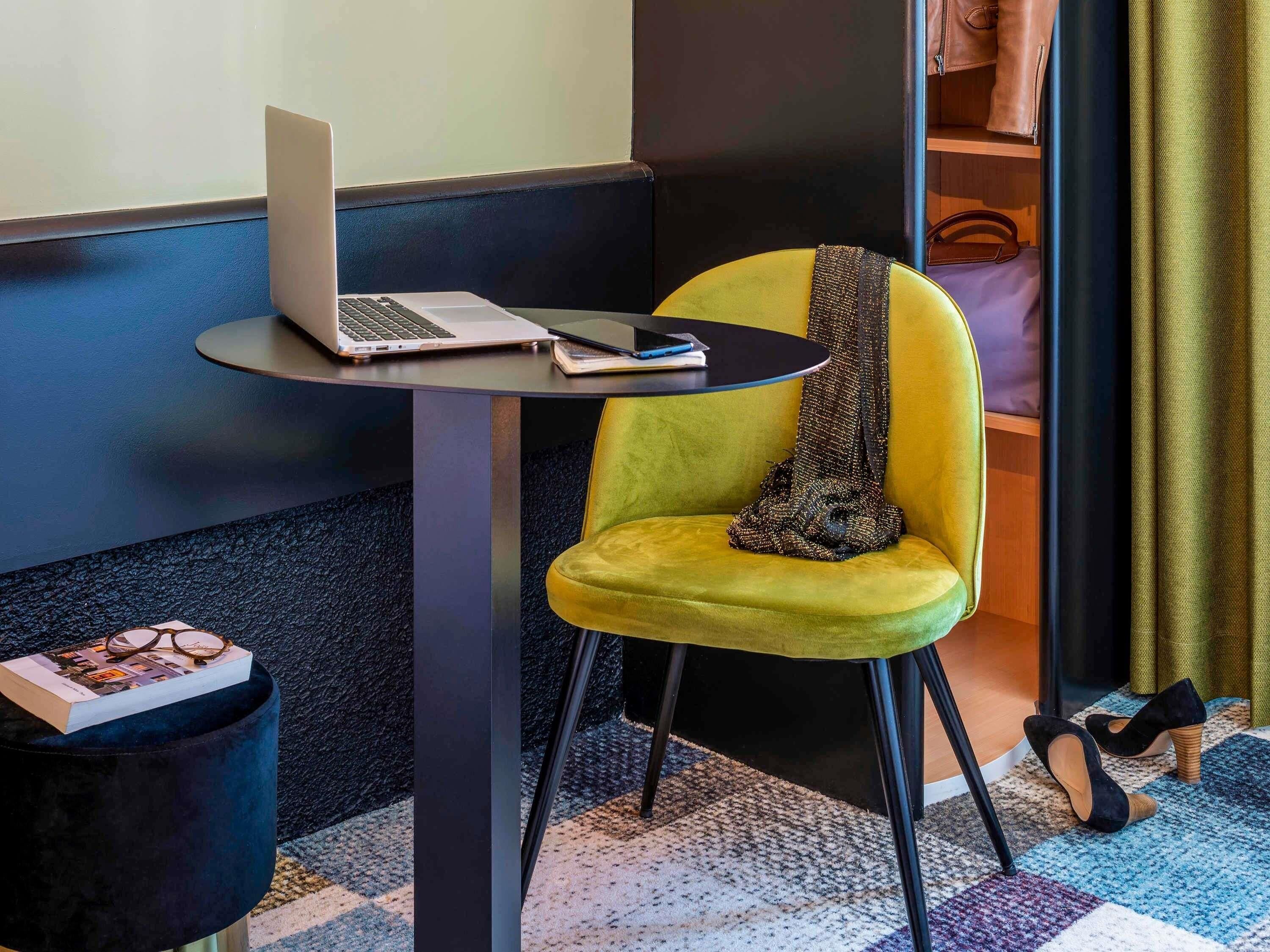 A modern room with a laptop on a small table, a yellow chair, a black trash bin, and a pair of shoes on the floor.