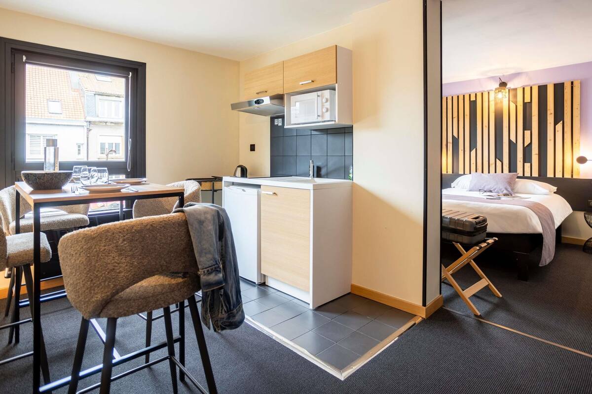 Una camera d'albergo compatta con angolo cottura, zona pranzo e un letto con testiera.
