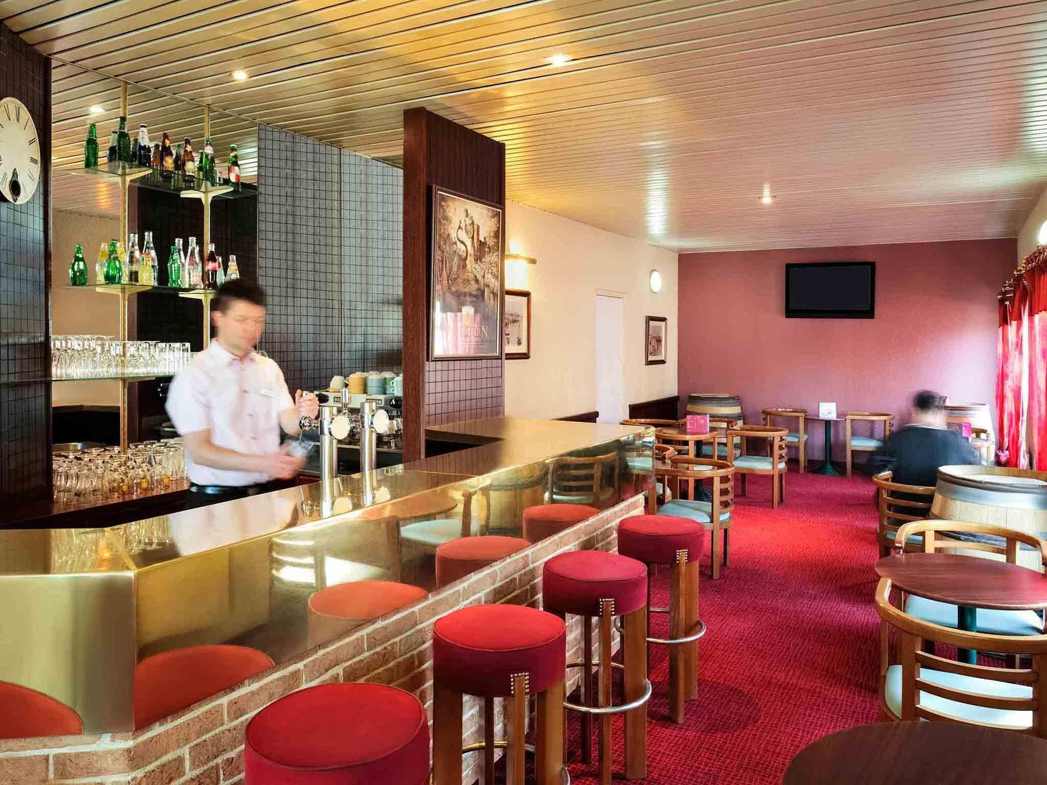 A bar area with stools, a bartender, and shelves with bottles.