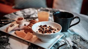 A breakfast setting with a bowl of cereal, a croissant, orange slices, and a glass of orange juice on a marble table.