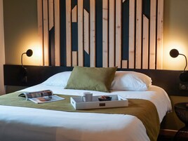 Una cama bien hecha con un almohadón verde, una bandeja con una taza y una taza de té, y una revista sobre la cama.