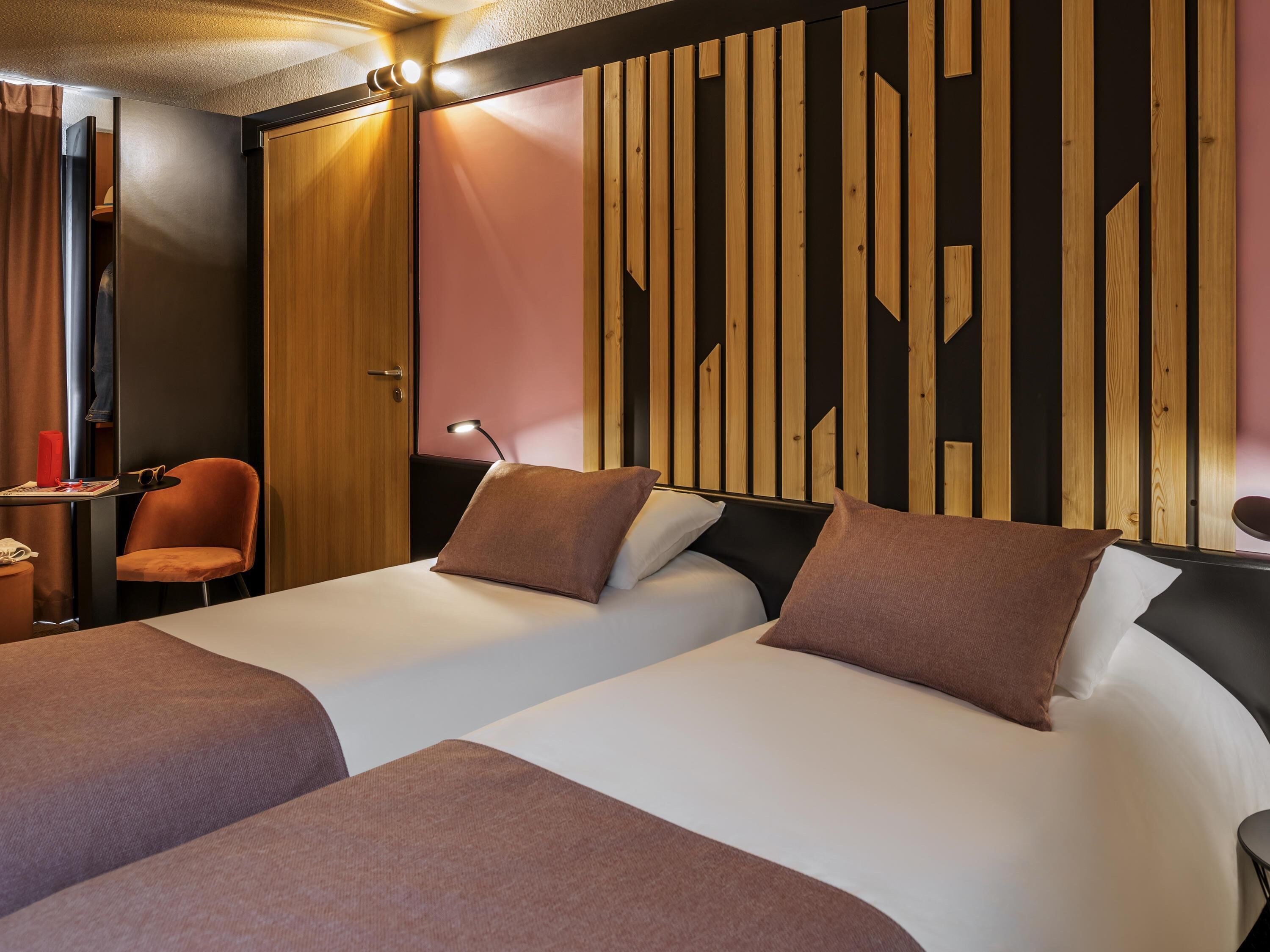 Habitación de hotel con dos camas, un escritorio, una silla y un armario.