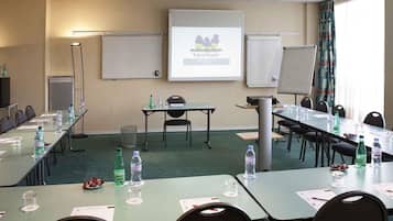 Une salle de conférence équipée de tables, de chaises, d’un écran de projection et d’un écran de présentation.