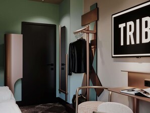 A hotel room with a bed, a desk with a chair, a coat rack with a jacket, and a door. - TRIBE Strasbourg Centre Gare (Opening Soon) (Strasbourg)