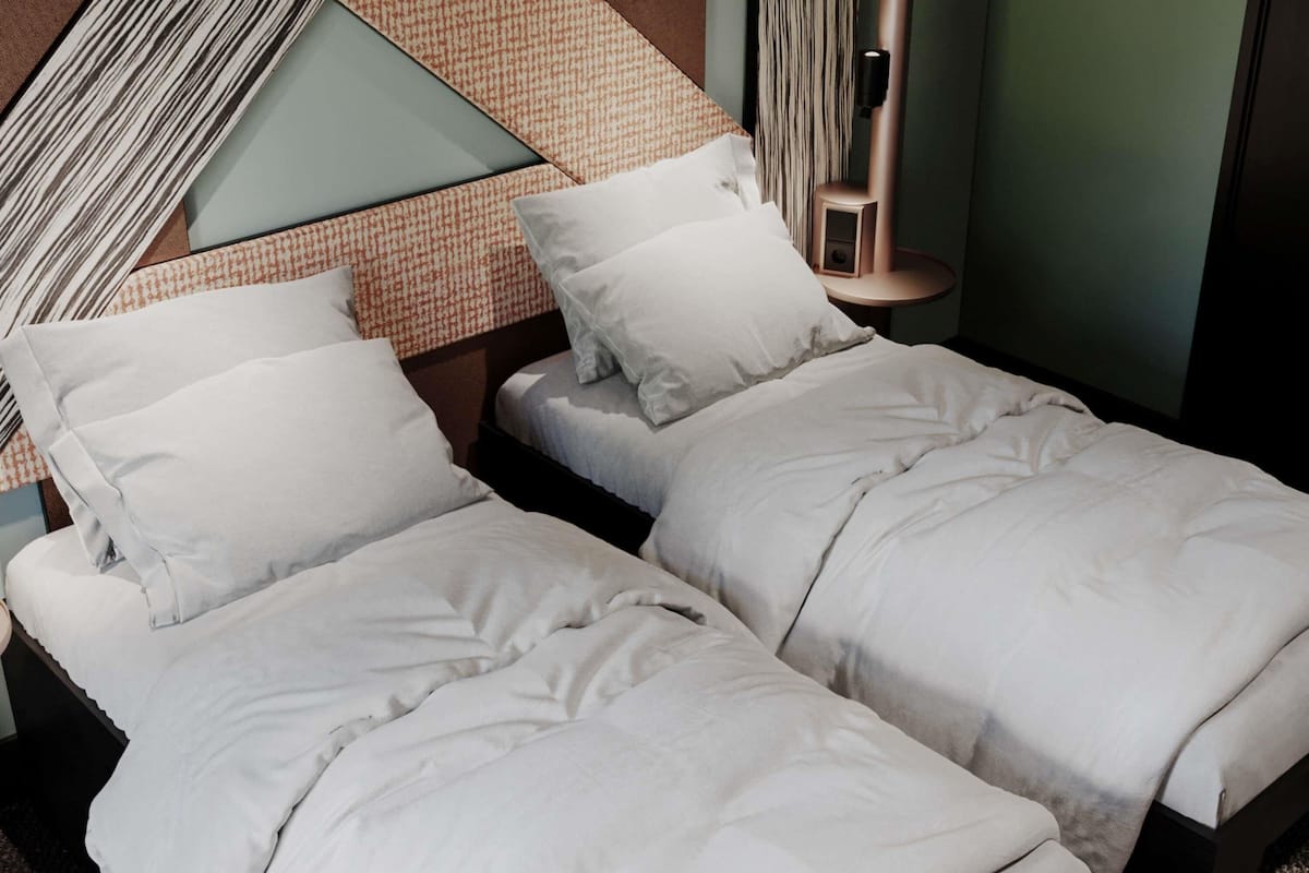 A modern hotel room with two single beds, a patterned wall, a tall bedside table, and a wall-mounted light fixture.