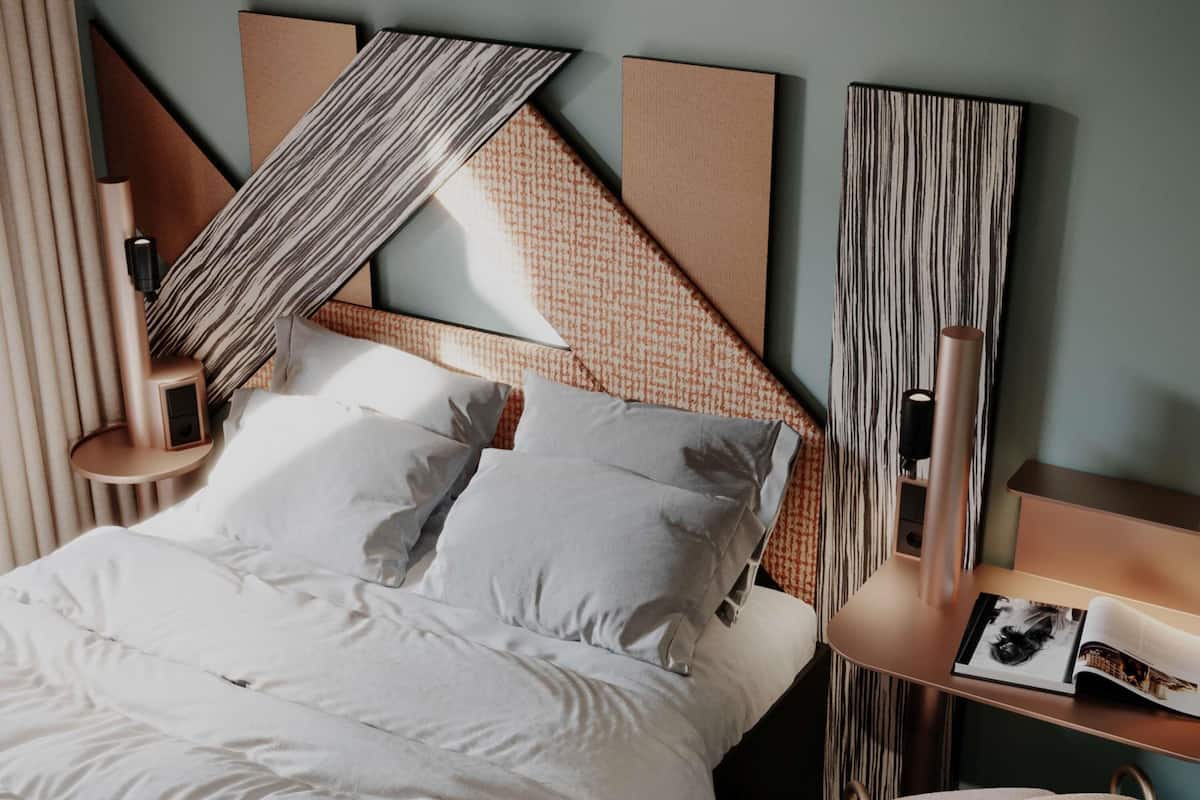A modern bedroom with a bed, pillows, a bedside table, a chair, and abstract wall art.