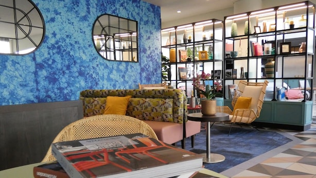 Un área de descanso moderna con un sofá, un sillón de mimbre y una mesita con libros.