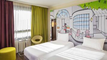 Une chambre d’hôtel avec deux lits, un pouf jaune, une chaise et une fresque murale.