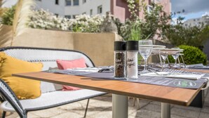 Un espace de restauration en plein air avec une table dressée pour deux personnes, comprenant un menu, des salières et des poivrières, et un verre d’eau.