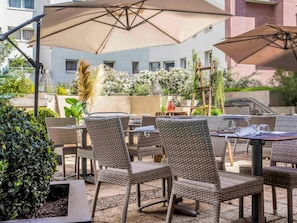 An outdoor seating area with wicker chairs and tables, umbrellas, and a brick building in the background. - ibis Styles Evry Courcouronnes Hotel and Events (Évry-Courcouronnes)