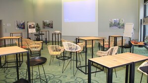 Un salón de conferencias con mesas, sillas, una pantalla de proyector y cuadros en las paredes.