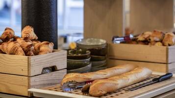 A wooden counter with bread and pastries, including croissants and baguettes, and a knife and tongs on a cutting board.