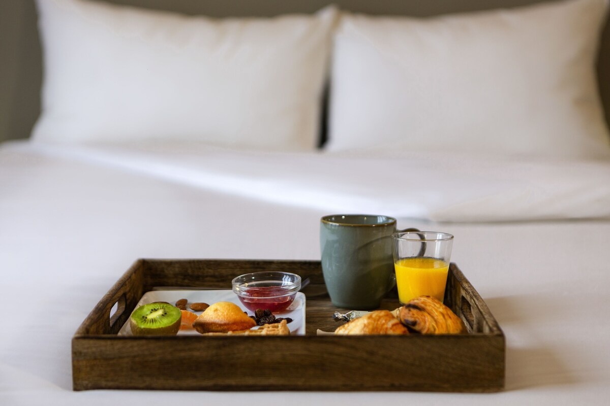 Bandeja de desayuno con frutas, bollería y bebidas sobre una cama.